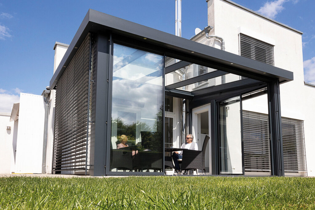 Terrassendach mit Glaswänden und Lamellen-Rollo vor einem modernen, weißen Haus in Fürth