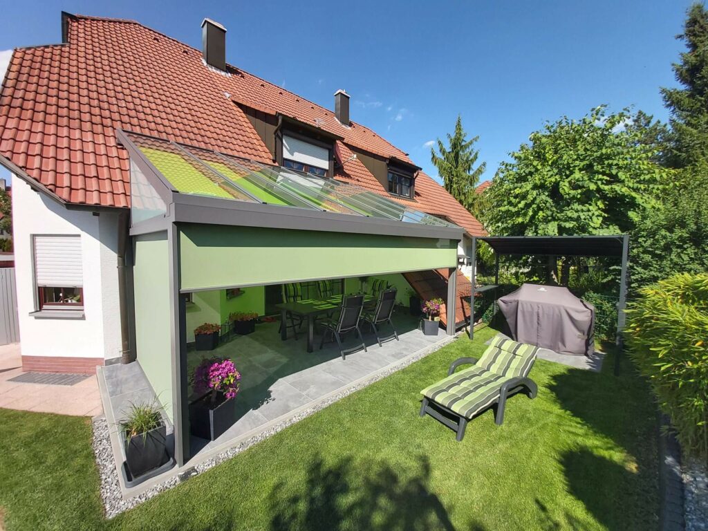 Überdachter Grill neben einer überdachten Terrasse mit grünen Textil-Screens. Geht mit etwas gutem Willen als Outdoor-Küche mit Dach durch.