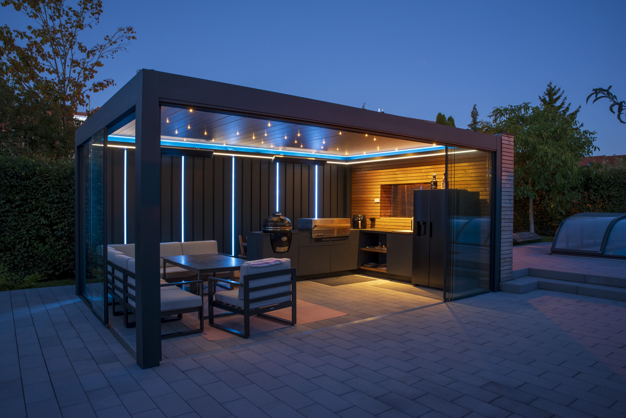blau beleuchtetes Poolhaus mit überdachter Outdoor-Küche am Abend mit blau-weißer LED-Beleuchtung