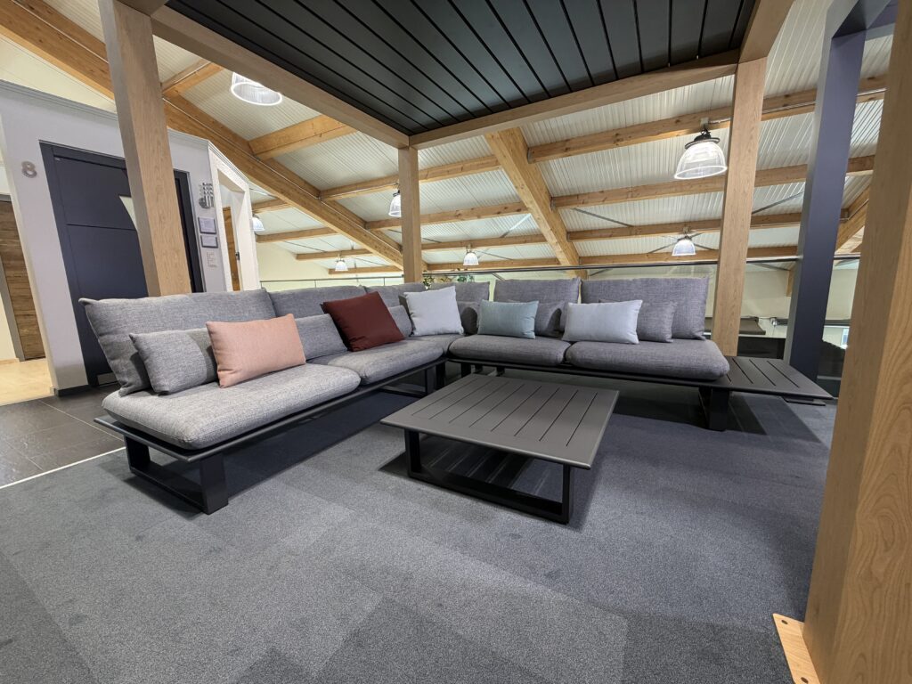 Outdoor-Lounge unter Terrassendach: Couchtisch und graues, L-förmiges Outdoor-Sofa der Marke K-Design.
