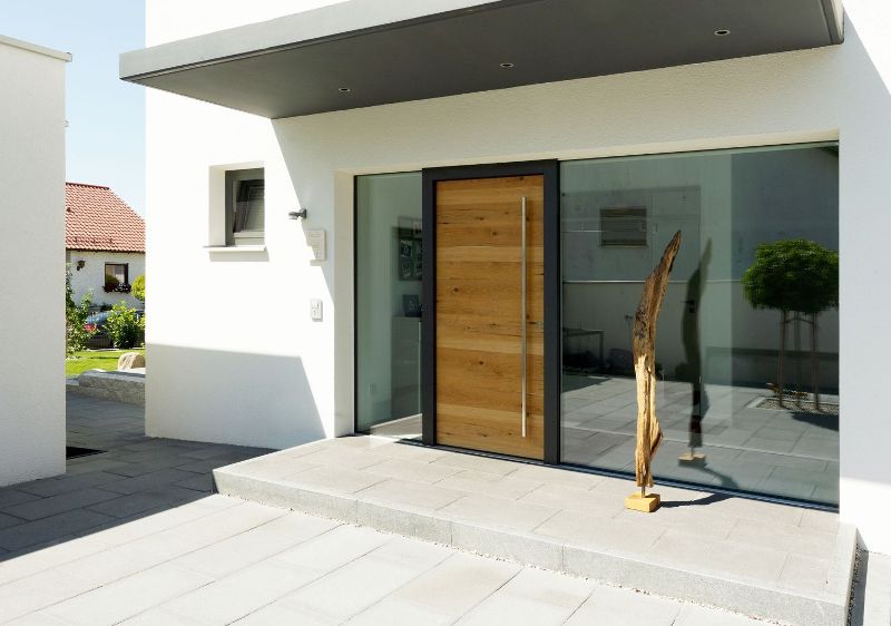 Moderne Holzhaustür bei Kutz mit natürlicher Holzoberfläche und großflächigen verglasten Seitenteilen an einem modernen Wohnhaus.