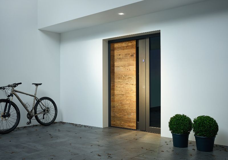 Minimalistisch gestaltete Holzhaustür bei Kutz mit natürlicher Holzoberfläche, dunklem Rahmen und verglastem Seitenteil.